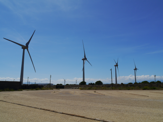 Vue panoramique par beau temps (ciel bleu). Il n'y a aucune voiture sur le parking. Une rangée d'éoliennes est placée en bordure du parking.